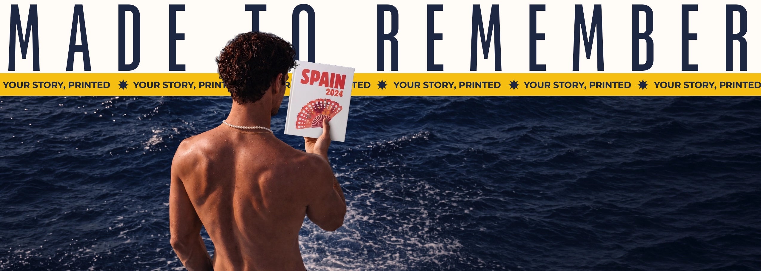 Man holding a book titled 'Spain' with ocean and 'Made to Remember' text in the background